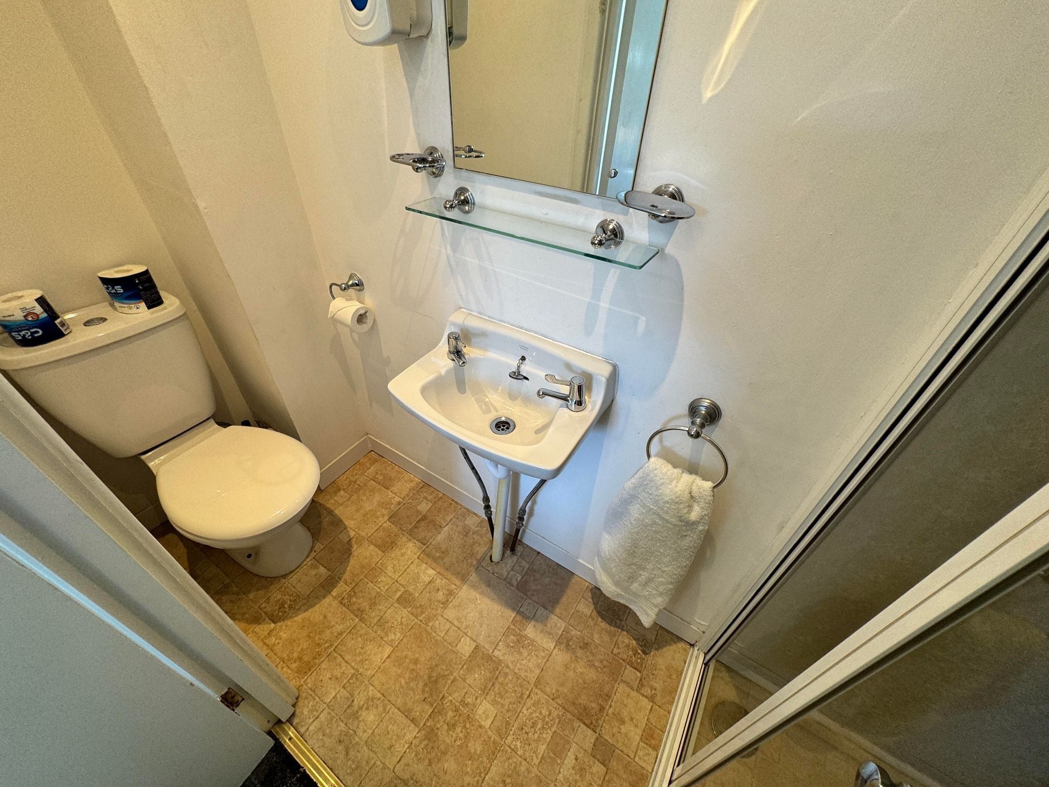 A compact bathroom with a toilet, sink, and glass shelf.