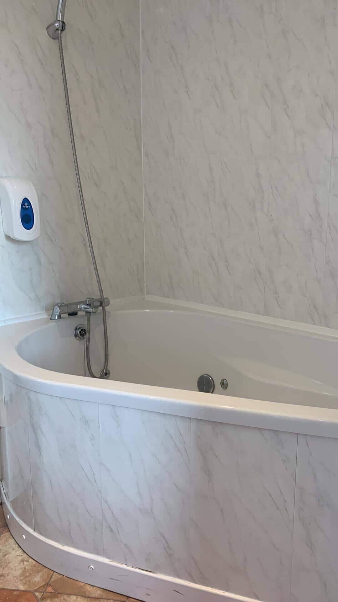 A bathroom with a bathtub, a shower, and a soap dispenser.