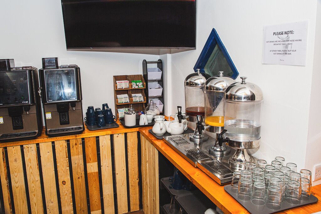Una estación de café con varias máquinas de café, un televisor montado en la pared y un cartel con instrucciones.