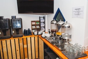 Una estación de café con varias máquinas de café, un televisor montado en la pared y un cartel con instrucciones.