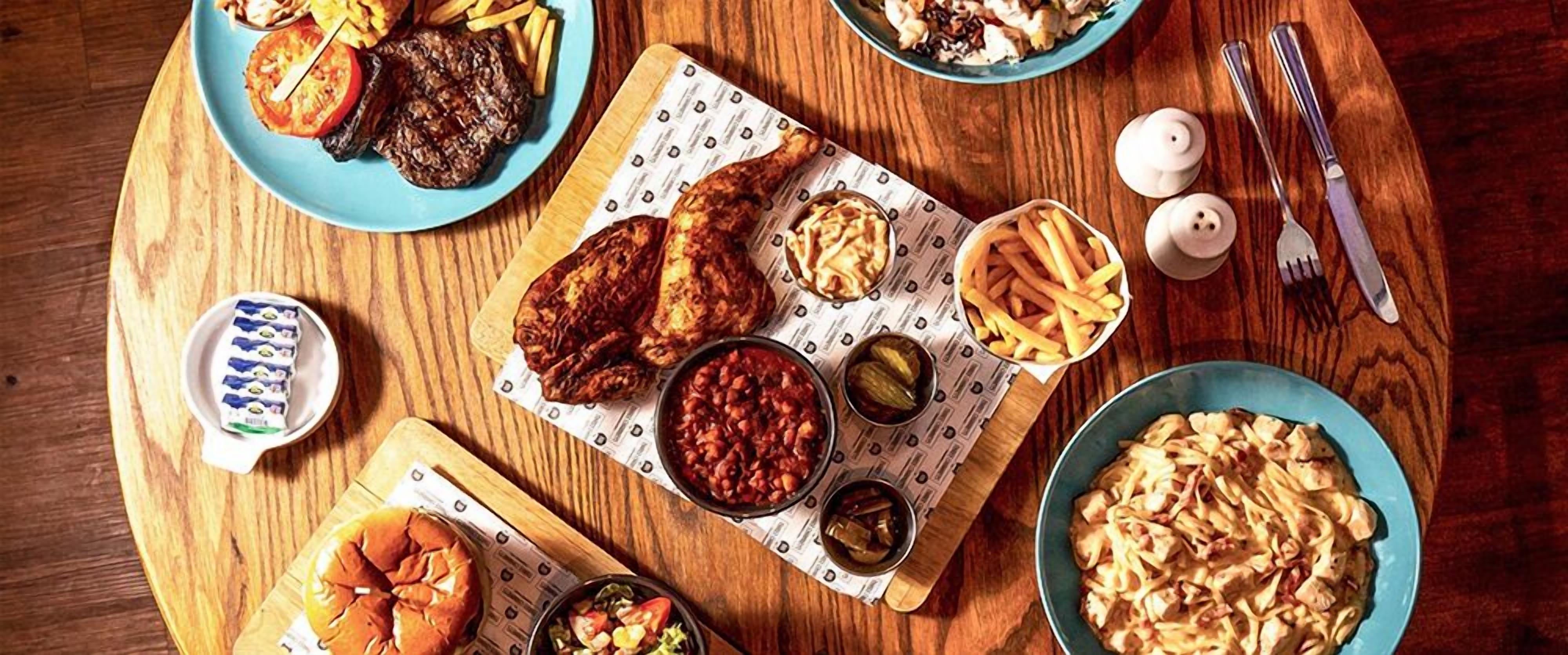 A wooden table with various food items including burgers, fries, and pasta.