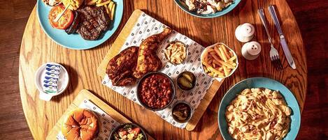 A wooden table with various food items including burgers, fries, and pasta.