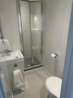 Un baño moderno con ducha de vidrio, lavabo con espejo e inodoro.