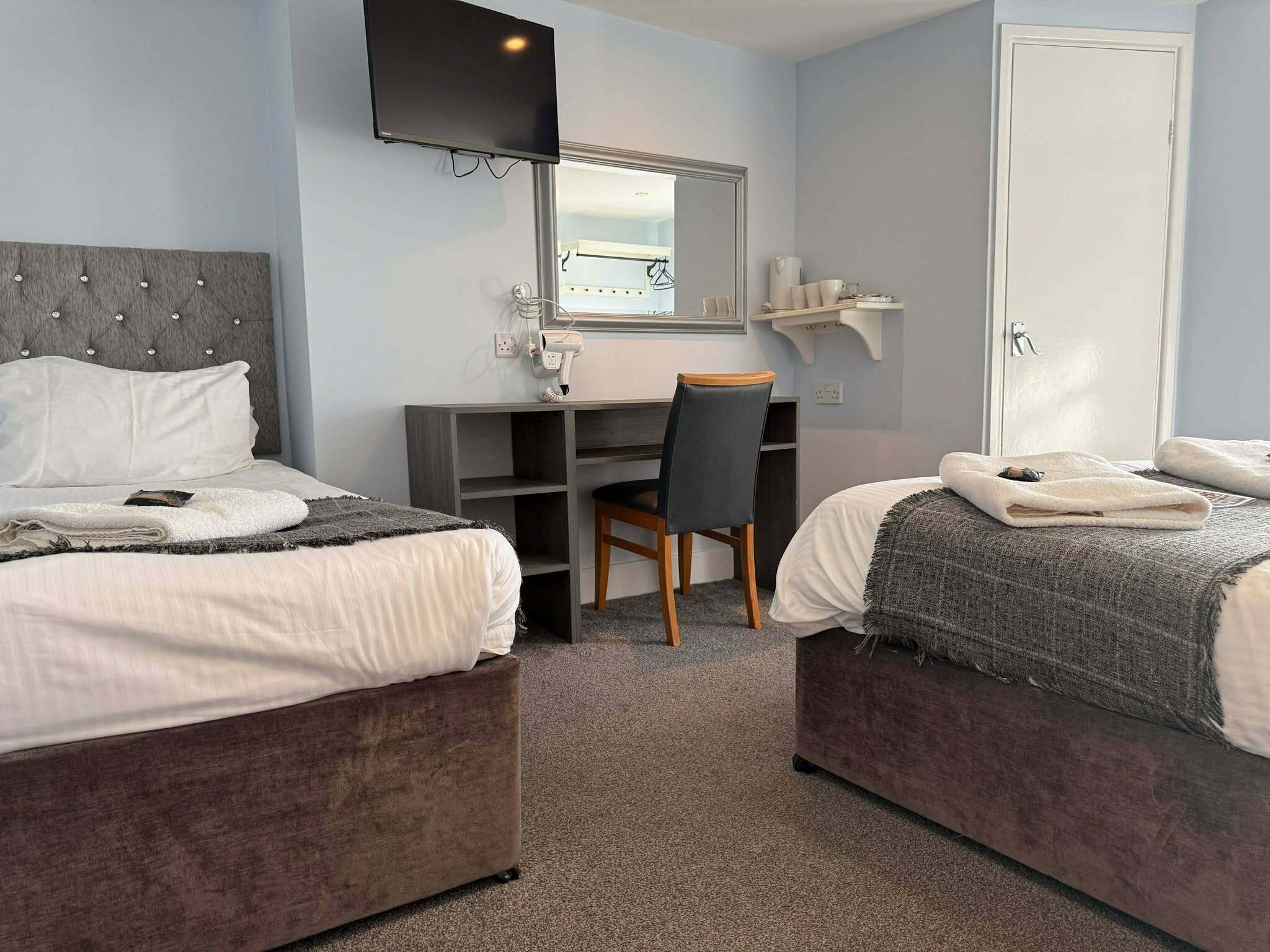 Ein Hotelzimmer mit zwei Betten, einem Schreibtisch, einem Stuhl, einem Fernseher und einem Kleiderschrank.