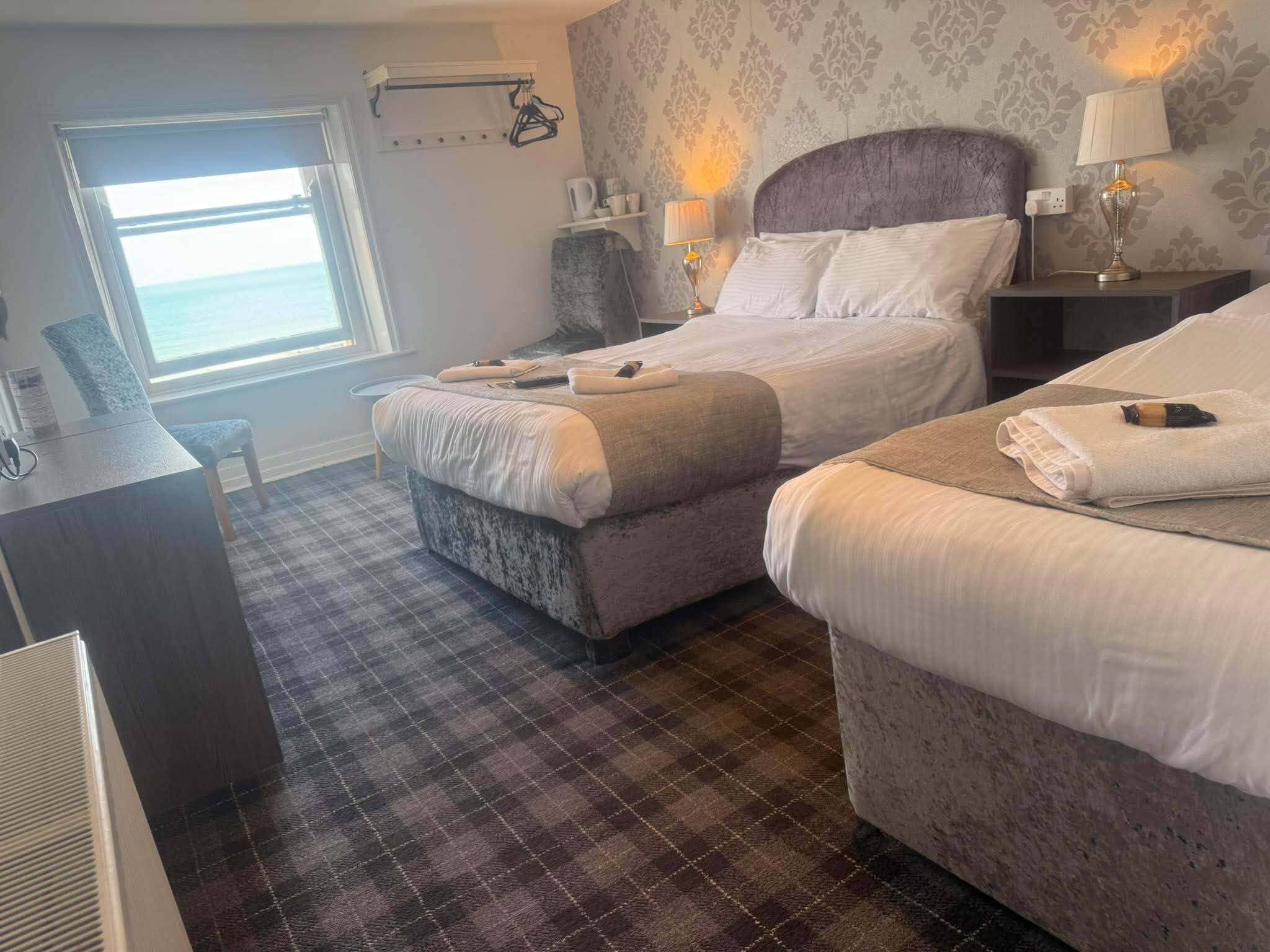 A hotel room with two beds, a desk, a chair, and a window with a view.