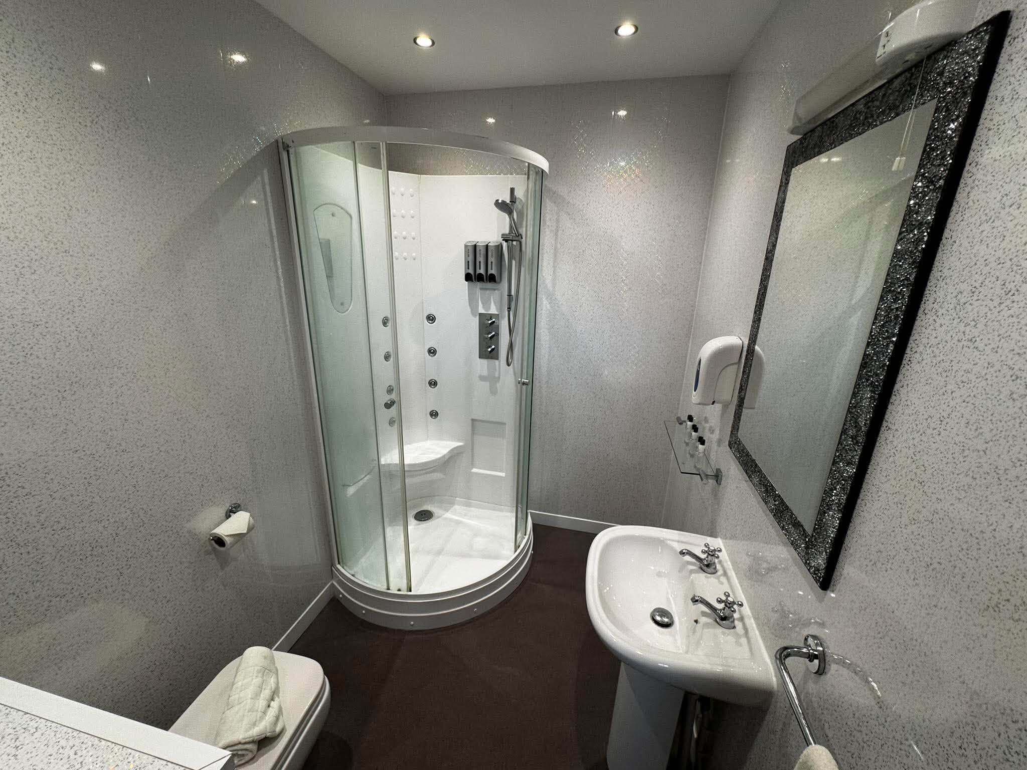 Un bany modern amb plat de dutxa tancat amb vidre, un lavabo sobre pedestal i un mirall gran.