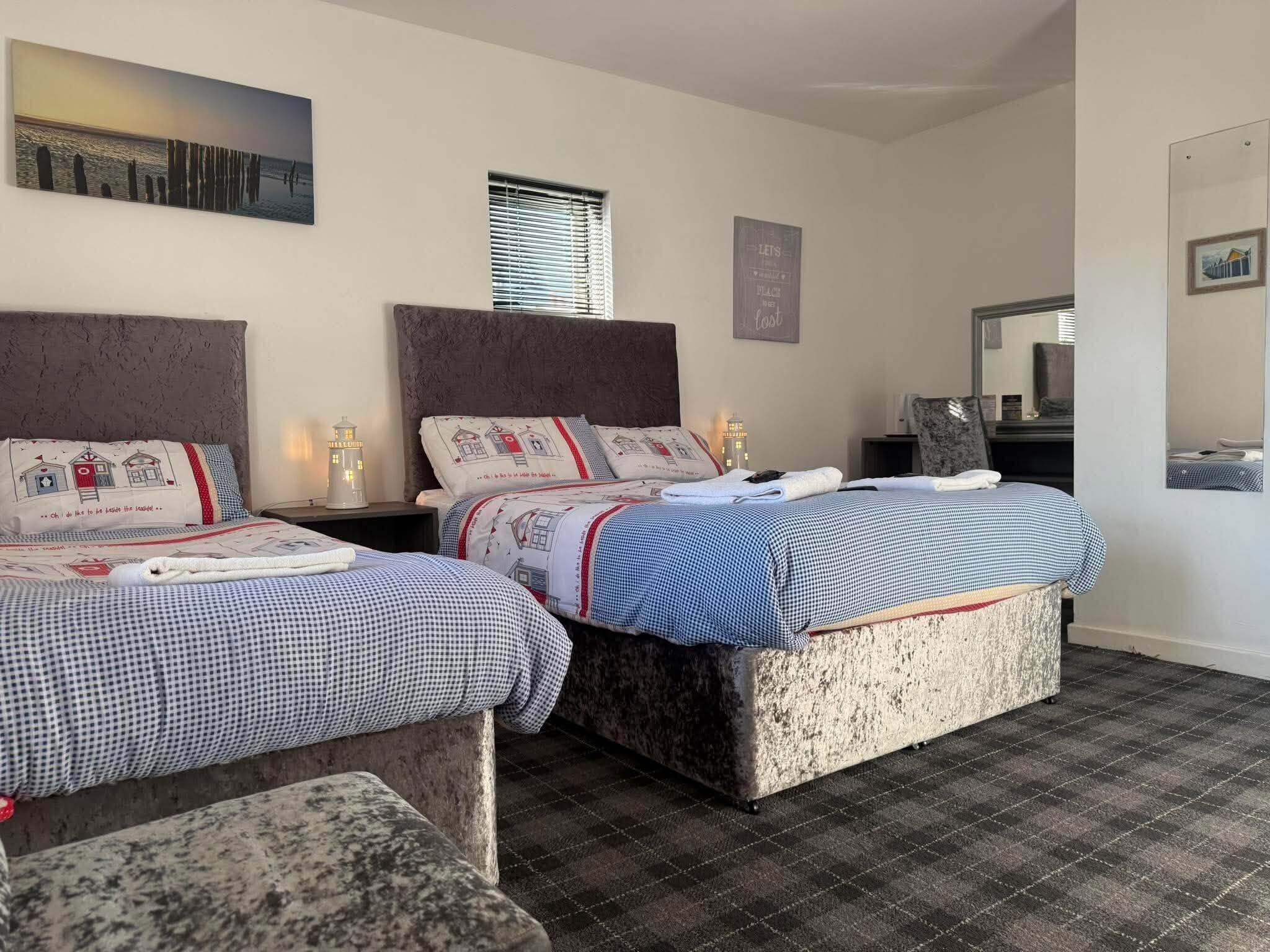 Una habitación de hotel con dos camas, un ventanal grande, un cuadro en la pared y un espejo.