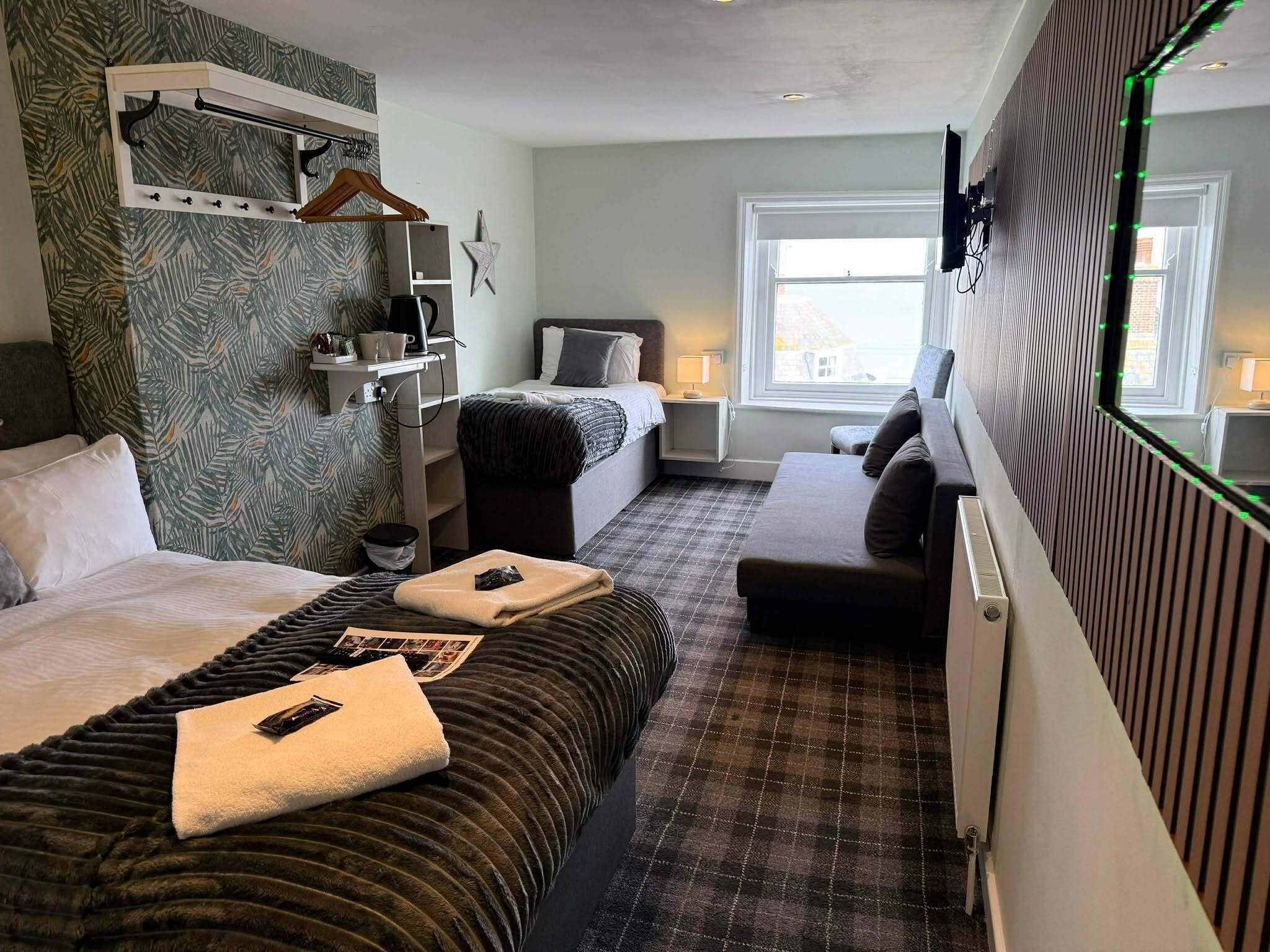 A hotel room with a bed, a sofa, a small table, a mirror, and a window.