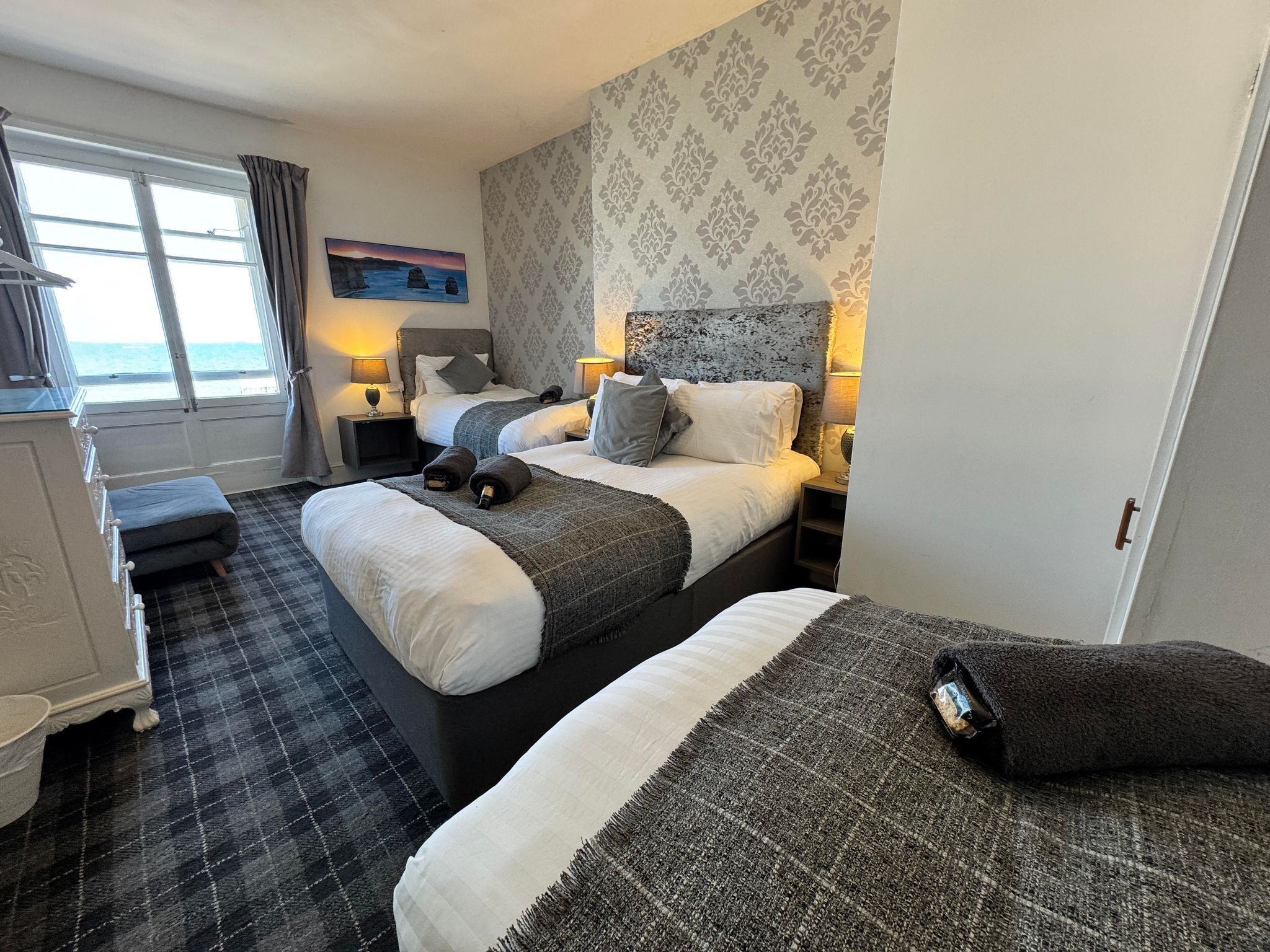 Een hotelkamer met twee bedden, een bureau en uitzicht op zee.