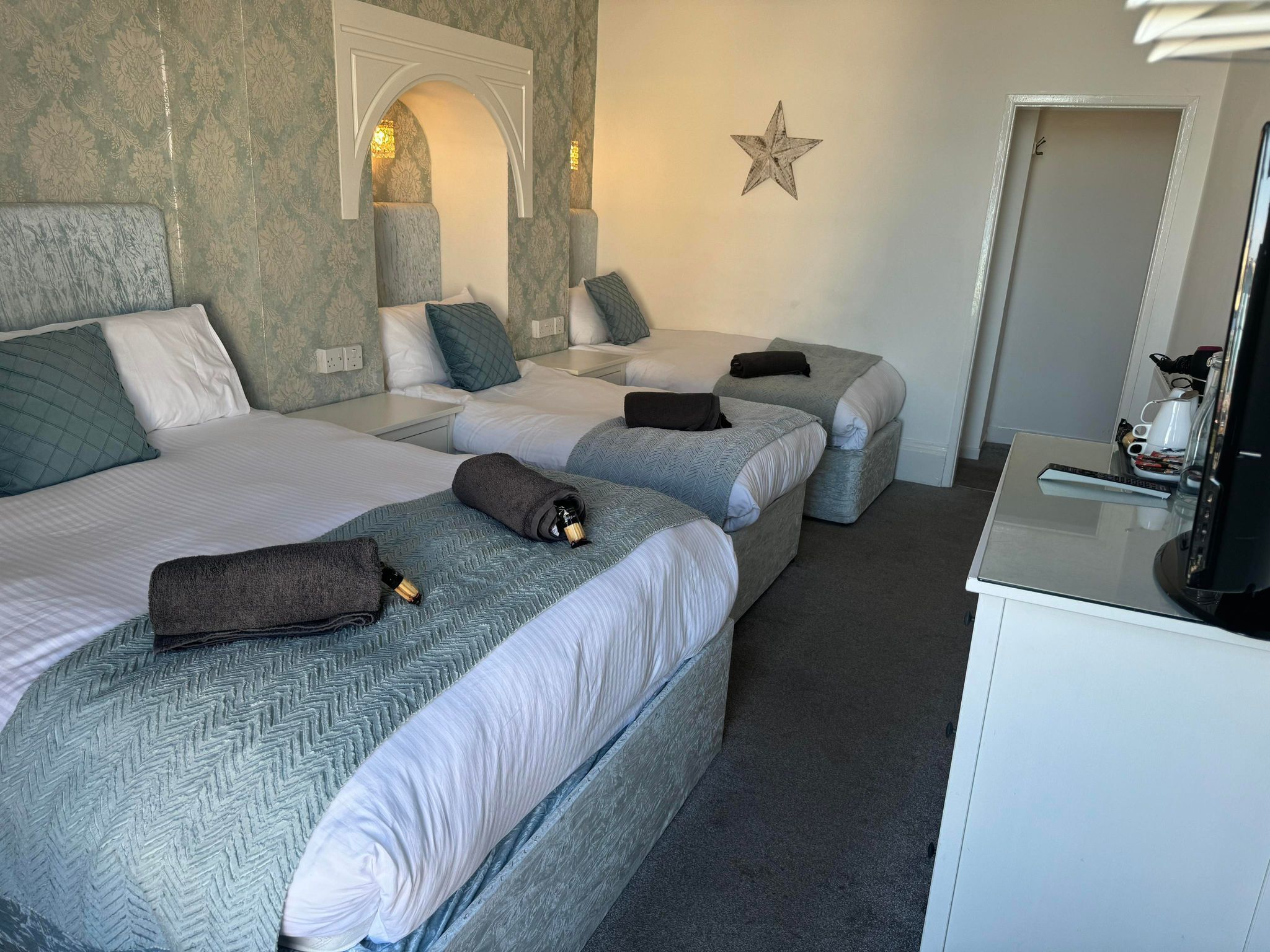 Habitación de hotel con tres camas, un escritorio y una televisión.
