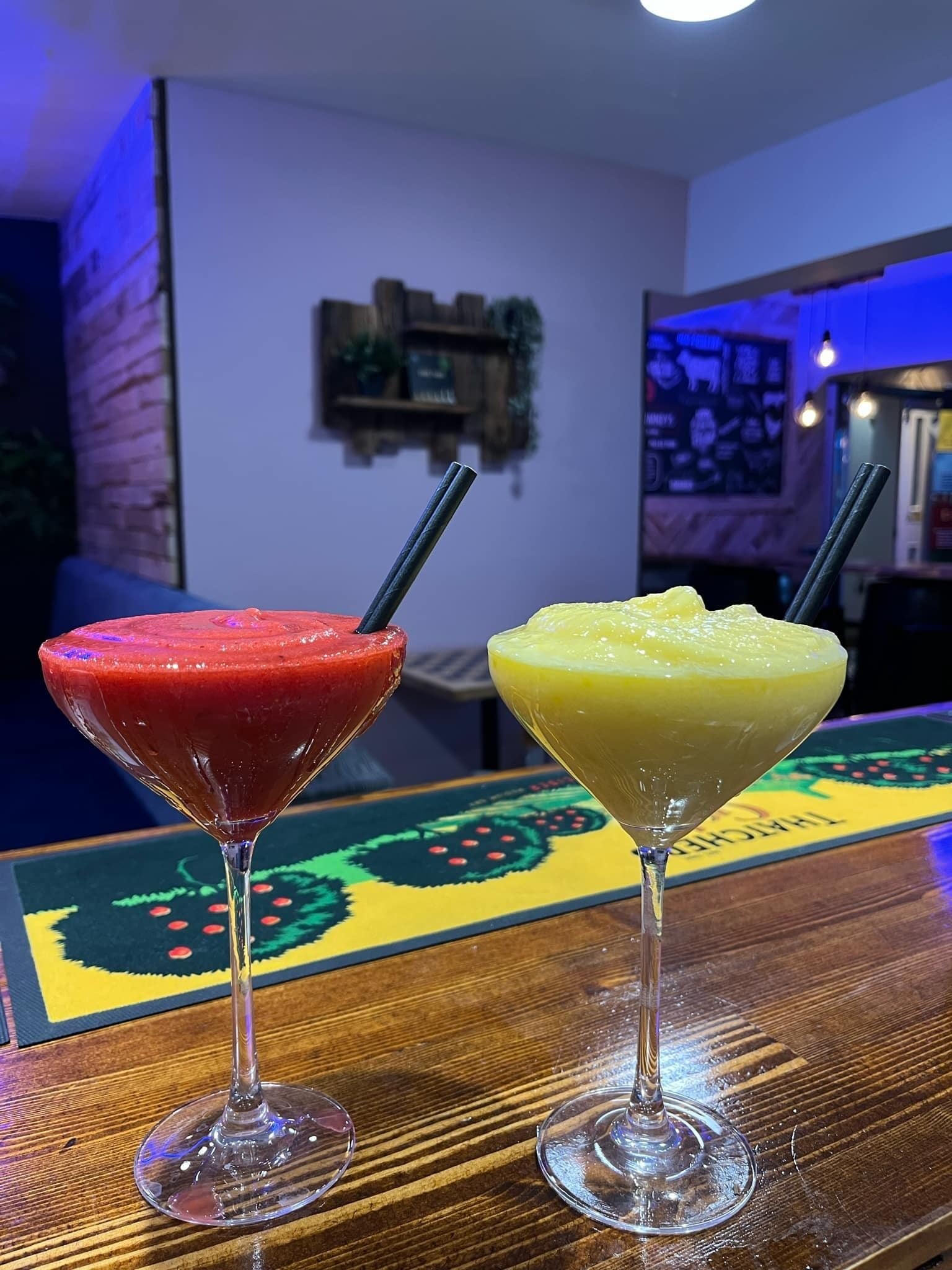 Two drinks in martini glasses on a wooden surface with a colorful tablecloth.