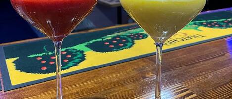 Two drinks in martini glasses on a wooden surface with a colorful tablecloth.