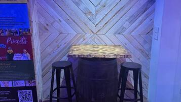 A wooden wall with a chevron pattern, a table with stools, and a sign with text and a QR code.