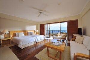 Habitación de hotel con dos camas, un sofá, un televisor y un balcón con vista al mar.