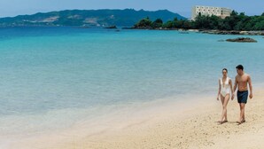A beach with clear water, a building on a hill, and a couple standing on the sand. - The Atta Terrace Club Towers (Onna)