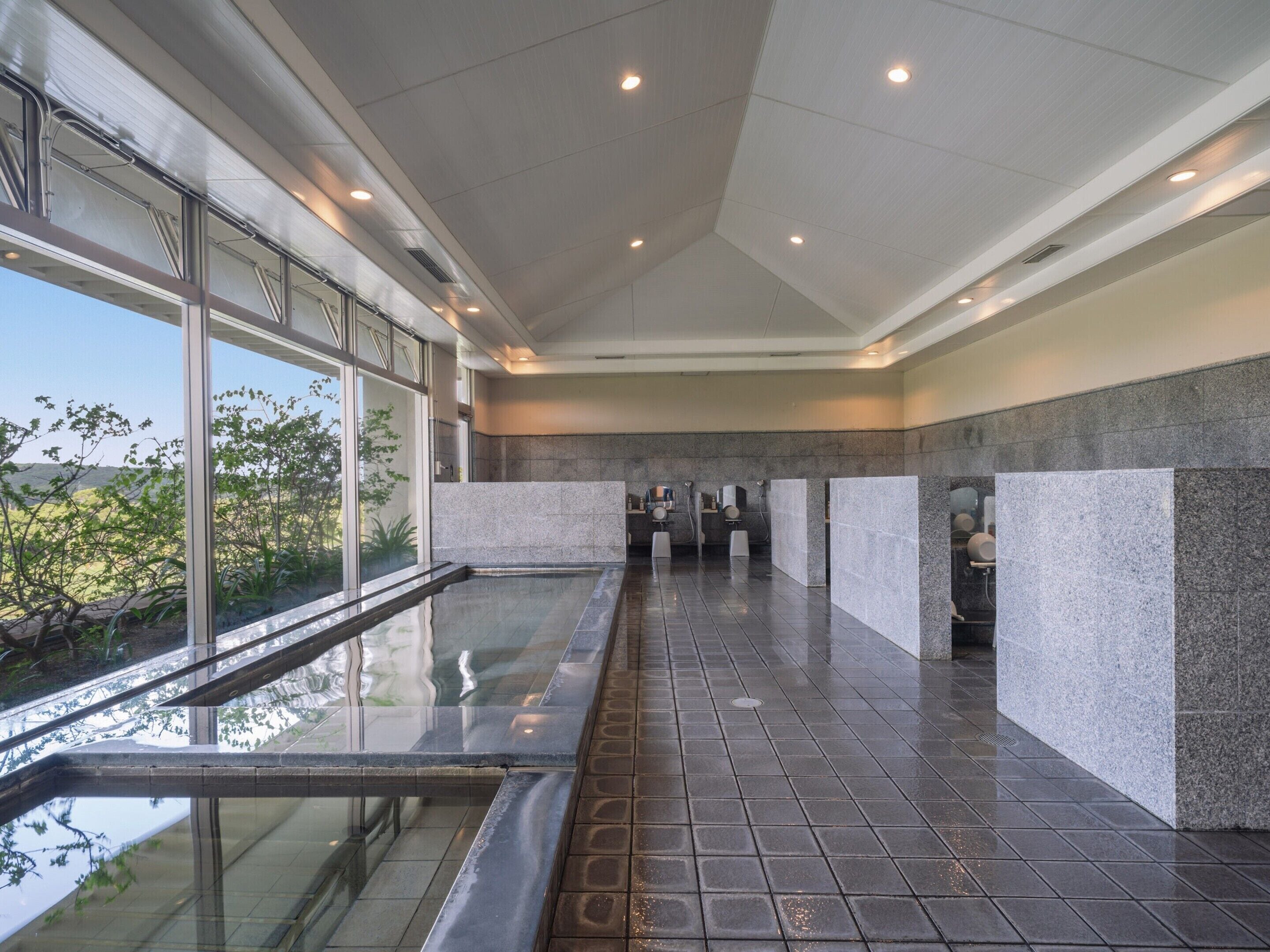 A modern indoor pool area with glass walls, a tiled floor, and a view of greenery outside.