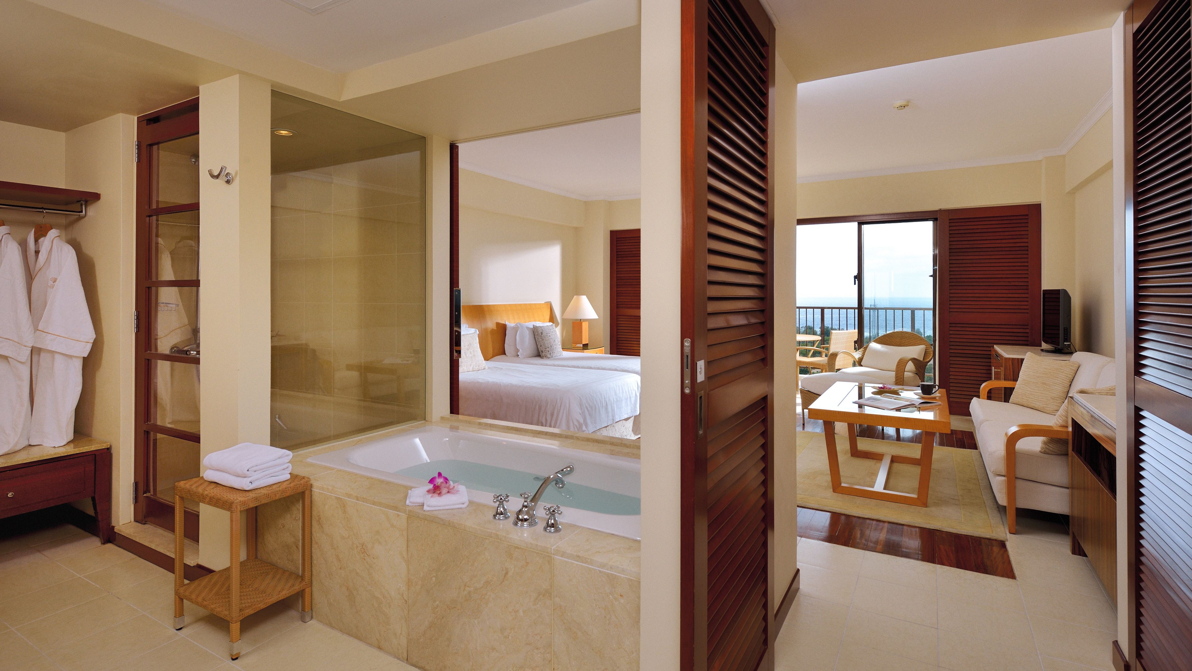 A hotel room with a large bathtub, a bed with two pillows, a desk with a chair, and a television.