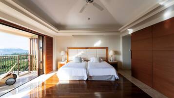 Une chambre spacieuse avec un grand lit, deux tables de chevet, un ventilateur de plafond et un balcon avec vue.