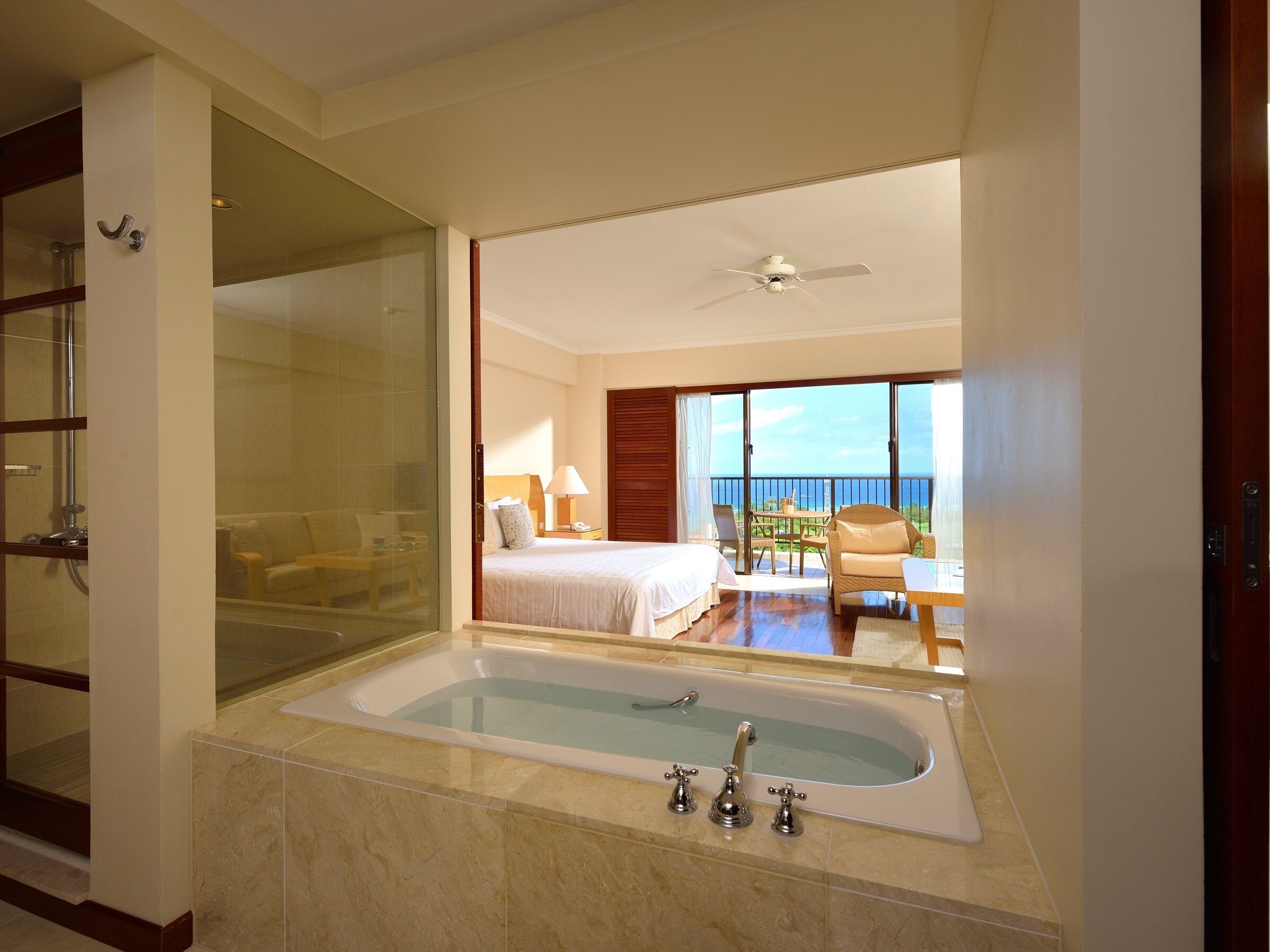 A hotel bathroom with a large bathtub, a glass shower enclosure, and a balcony with a view.
