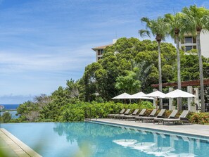 A swimming pool with lounge chairs and umbrellas, surrounded by lush greenery and a building in the background. - The Atta Terrace Club Towers (Onna)