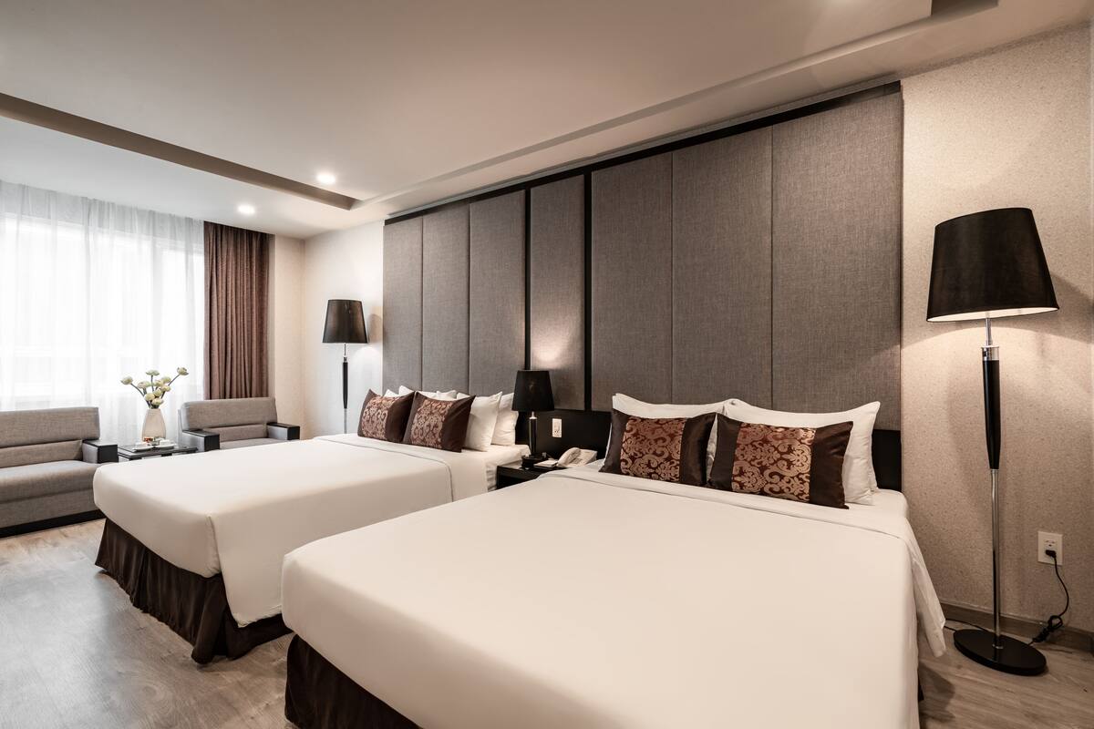 A hotel room with two beds, a sofa, a desk, and a lamp.
