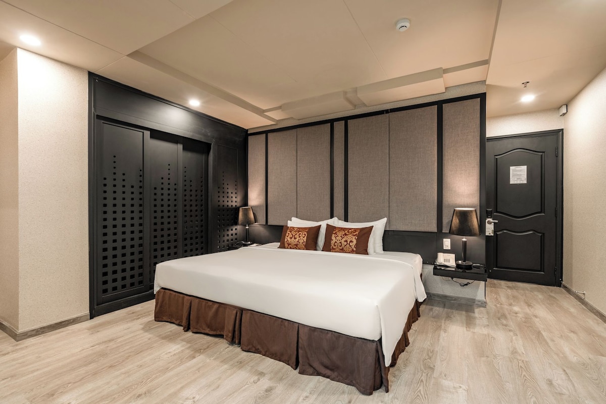 A hotel room with a large bed, a desk with a telephone, and a door with a security camera.