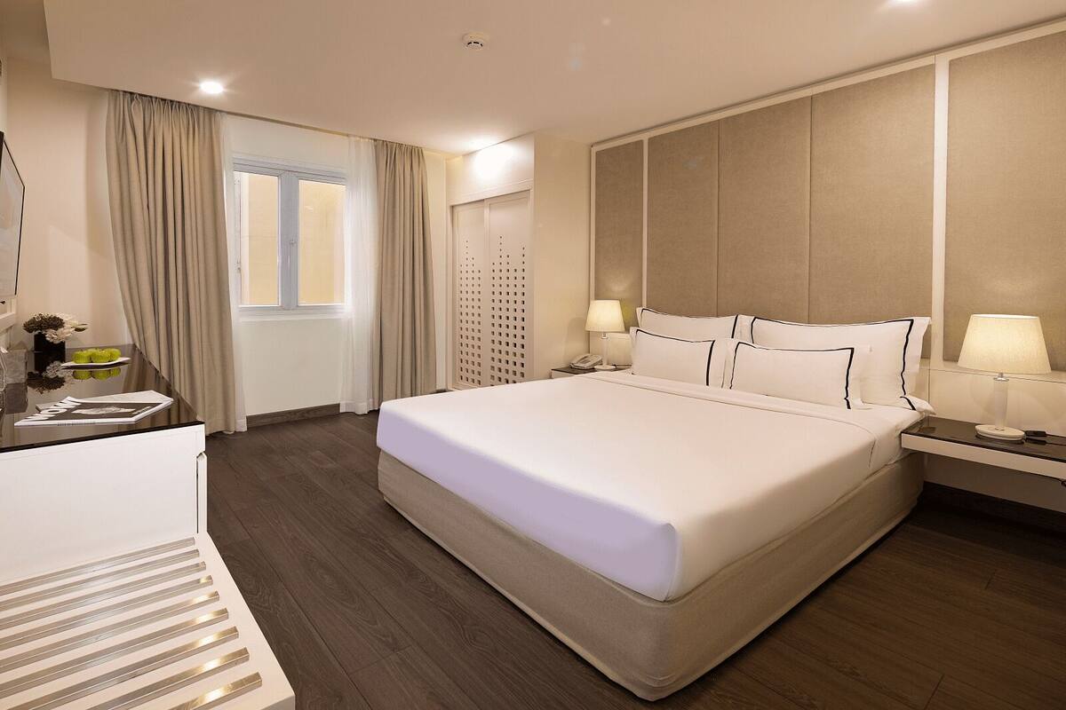 A hotel room with a large bed, bedside tables, a desk, and a window with curtains.