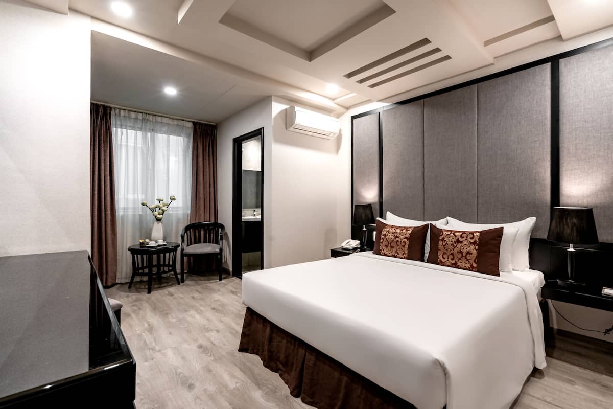 A hotel room with a large bed, a desk, a chair, and a small table with a vase of flowers.