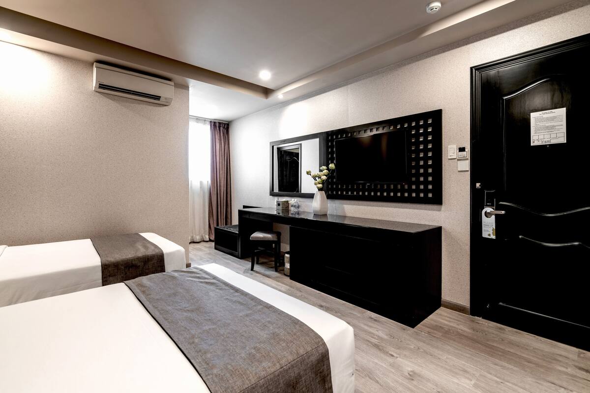 A hotel room with two beds, a desk, a mirror, and a door.