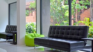 A modern living room with a black leather sofa, a green bean bag, and a glass coffee table. - Art Hotel Chaweng Beach (Koh Samui)