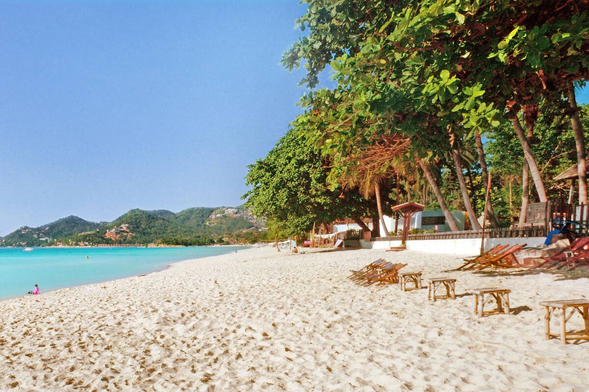 A beach with clear turquoise water, sandy shore, and wooden beach chairs.