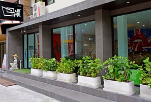 A modern hotel exterior with a sign reading "Art Hotel," large windows, and potted plants along the entrance.