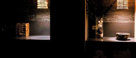 A dimly lit room with a bed, a small table with a vase of flowers, and two hanging light fixtures.