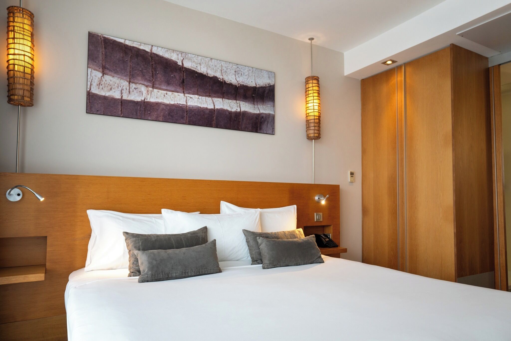 Habitación de hotel con una cama grande, cabecera de madera, un cuadro abstracto en la pared y una mesita de noche con lámpara.