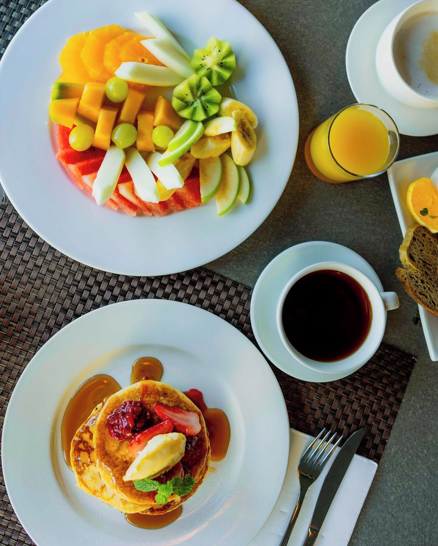 A breakfast setting with a plate of pancakes topped with strawberries and a side of fruit salad.