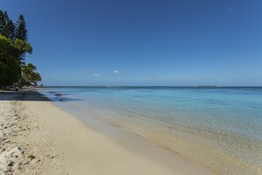 Une plage à l’eau claire, avec un rivage sablonneux et une île qui se profile à l’horizon.