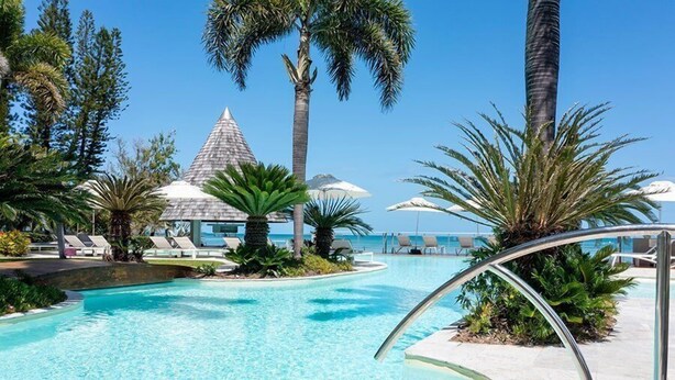 A pool area with lounge chairs, palm trees, and a building with a conical roof. - Chateau Royal Beach Resort and Spa (Nouméa)