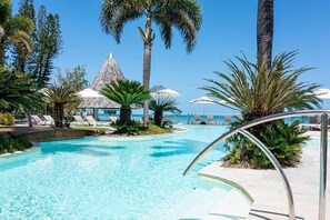 A pool area with lounge chairs, palm trees, and a building with a conical roof. - Chateau Royal Beach Resort and Spa (Nouméa)