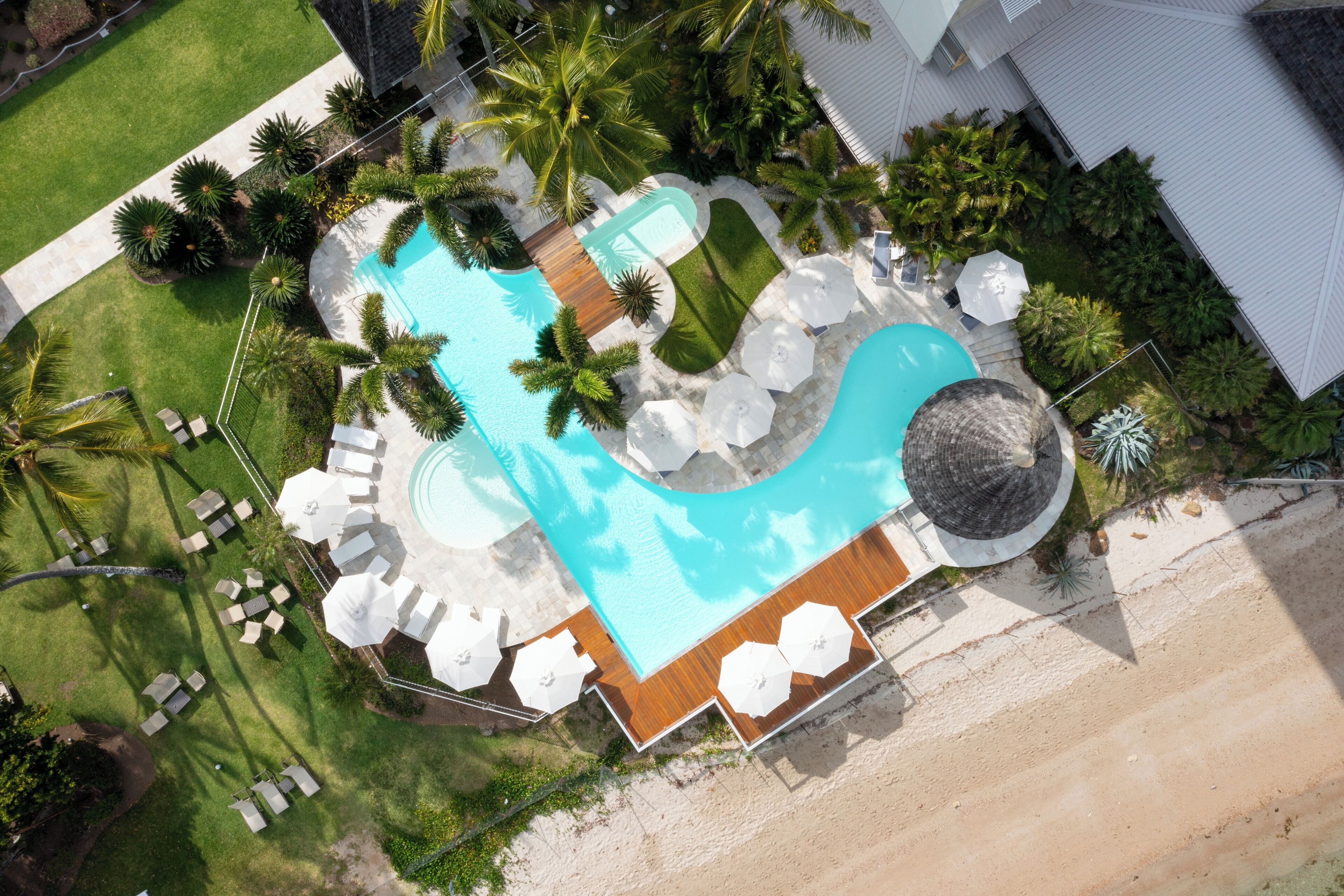 Vista aérea de un complejo turístico con una gran piscina, tumbonas y palmeras.