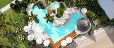 Vista aérea de un complejo turístico con una gran piscina, tumbonas y palmeras.