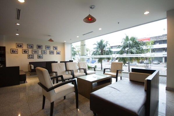 A hotel lobby with a reception desk, seating area, and large windows offering a view of the street and palm trees.