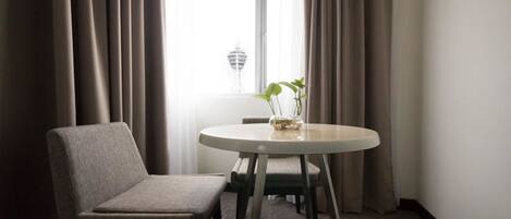 A room with a round table, a chair, and a window with curtains.