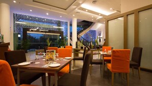 A modern dining area with orange chairs and tables, a large window with a view, and decorative lighting on the ceiling. - StarCity Hotel Alor Setar (Alor Setar)