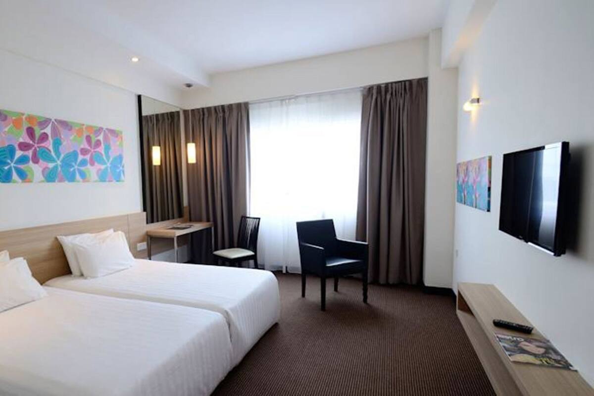 A hotel room with two beds, a desk, a chair, a TV, and a colorful abstract painting on the wall.