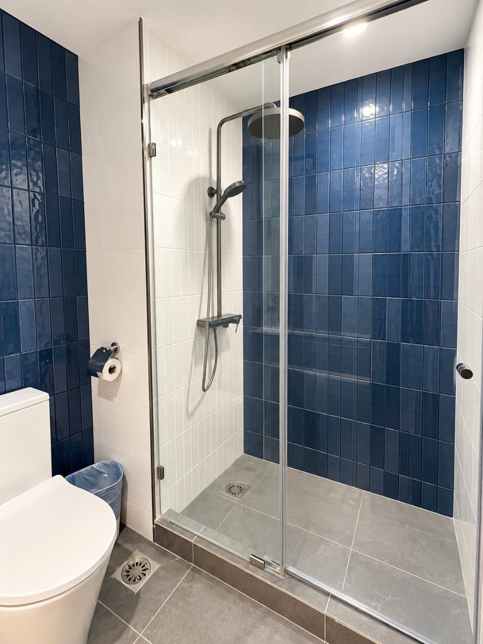 A bathroom with a glass-enclosed shower, white toilet, and blue-tiled walls.