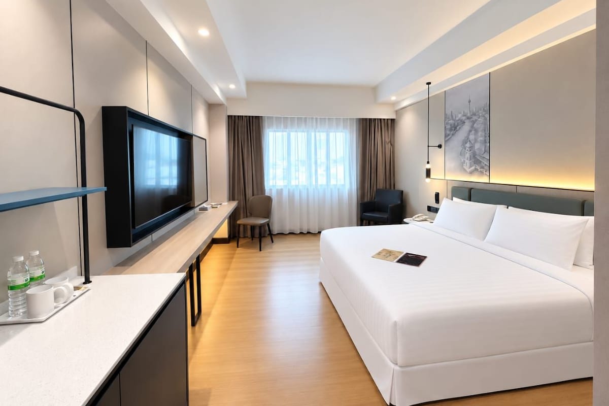 Ein modernes Hotelzimmer mit einem großen Bett, einem Flachbildfernseher, einem Schreibtisch mit Stuhl und Blick auf die Stadt durch das Fenster.