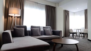 A modern hotel room with a sectional sofa, a round coffee table, and a desk with two chairs. - StarCity Hotel Alor Setar (Alor Setar)