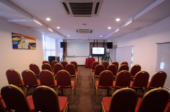 A conference room with rows of chairs facing a projection screen, a podium, and a painting on the wall.