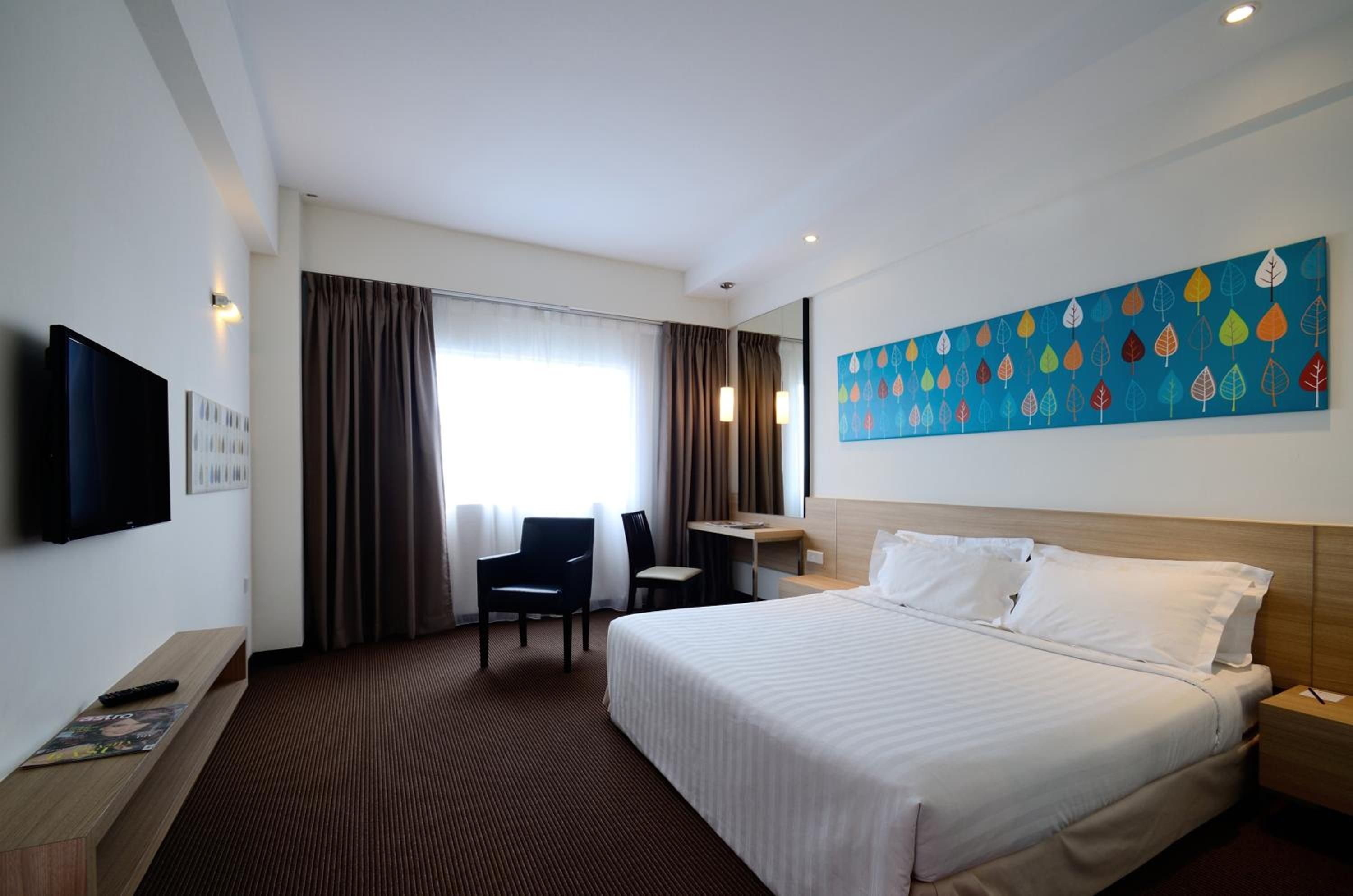 A hotel room with a bed, a desk, a chair, a television, and a painting on the wall.