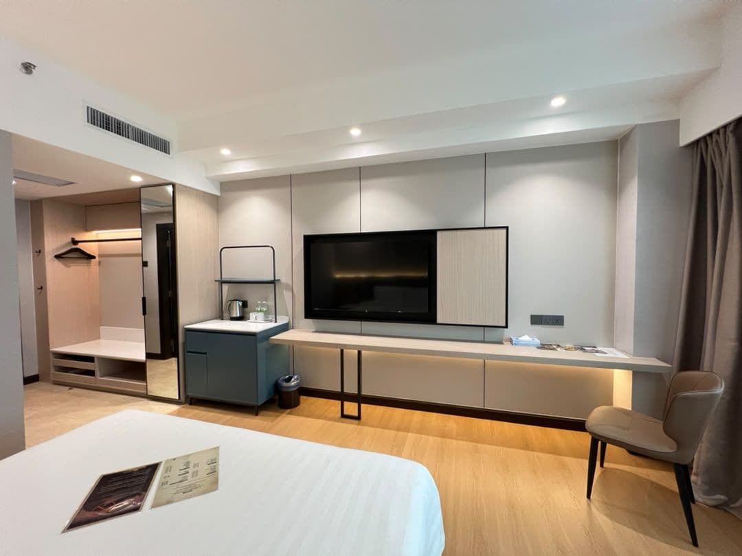 Una habitación de hotel moderna con cama, escritorio, televisor de pantalla plana, espejo y silla.
